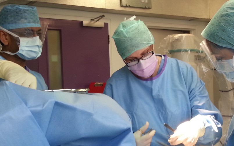 A surgeon is wearing blue and has a mask on.
