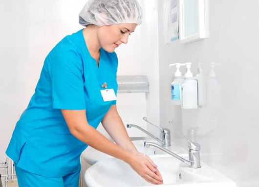 A woman in blue scrubs washes her hands.