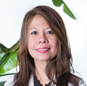 A woman with long brown hair wearing a white lab coat.