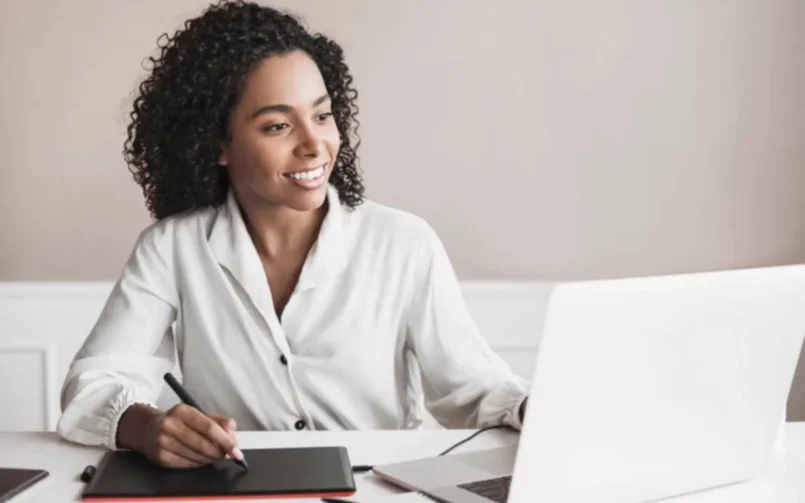 Smiling woman working on laptop and tablet.